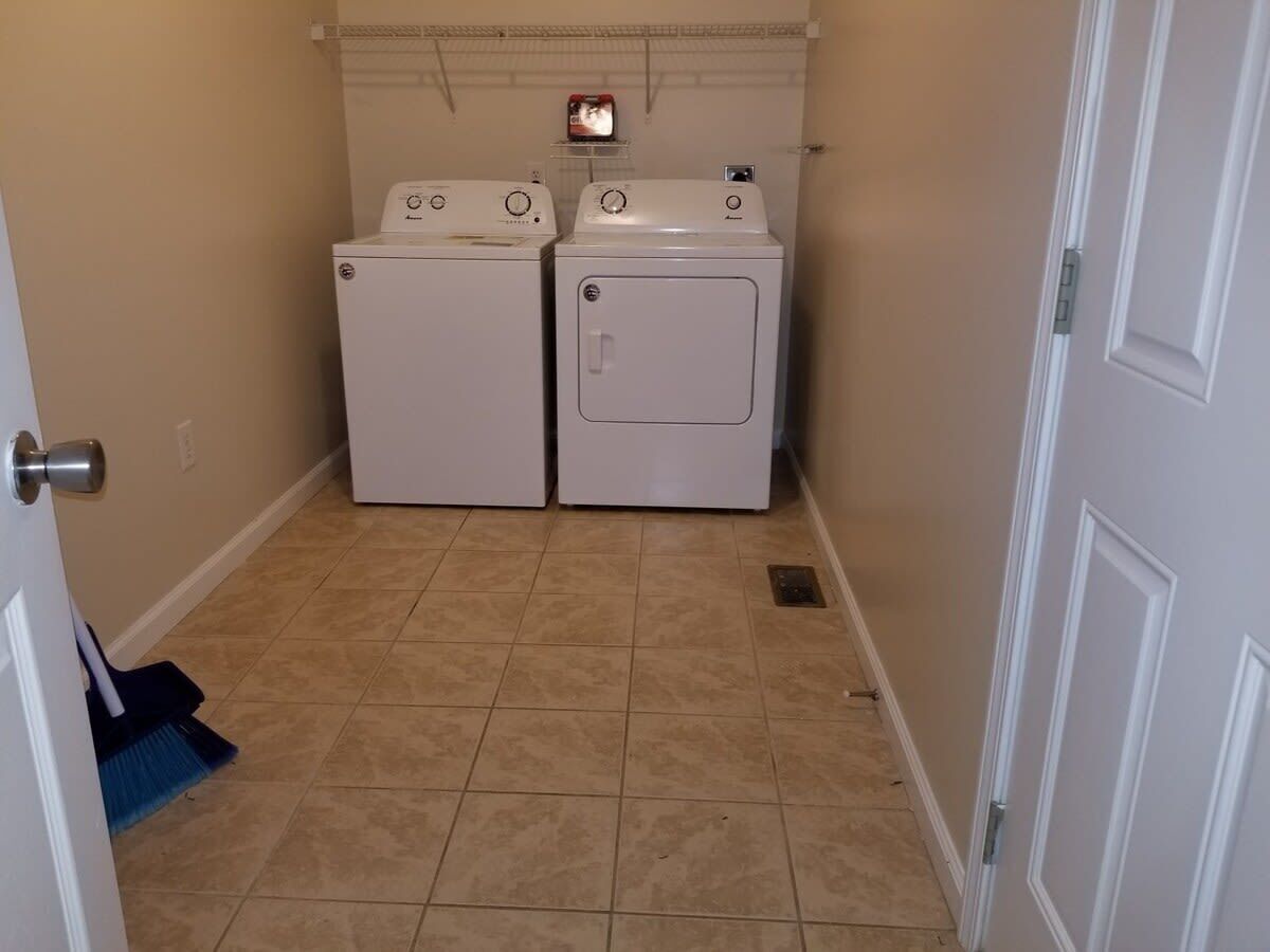 A laundry room with two stacked washers and dryers, a broom, and a tiled floor.