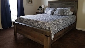 A bedroom with a wooden bed, patterned bedspread, and a nightstand with a lamp and a plant. - Spacious 3BR 2BA, 11 Min to Cummins Falls Park (Cookeville)