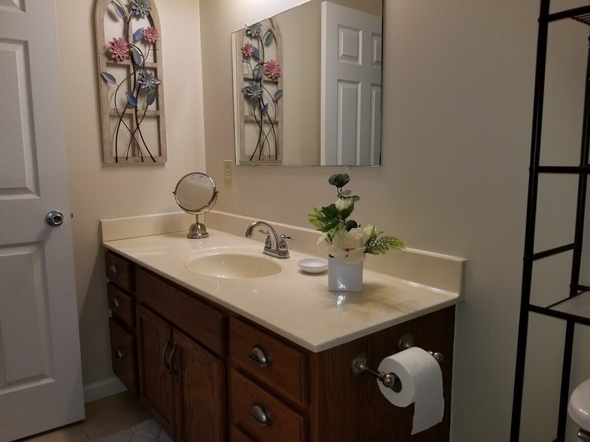Un baño con lavamanos doble, armarios de madera, un espejo y un dispensador de papel higiénico.
