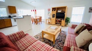 A living room with a sofa, a coffee table, a TV stand, and a dining area with chairs and a table. - Gorgeous Views From Pool! 3 Bedroom Home by RedAwning (Haines City)