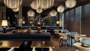 Ein modernes Restaurant mit dunklem Interieur, blauen Sitzmöglichkeiten und mehreren hängenden Leuchten.
