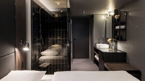 Ein modernes Hotelzimmer mit einem großen Bett, einer separaten Dusche, einem Schminktisch mit Spiegel und einer kleinen Sitzecke.