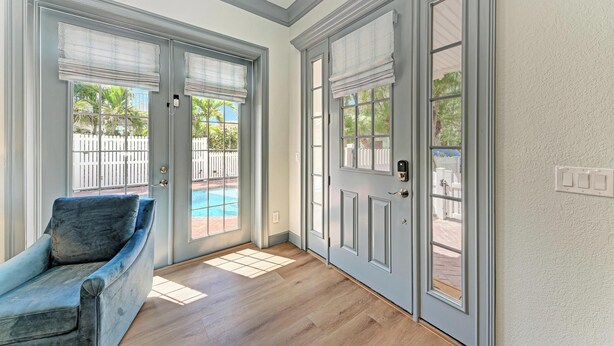 Una habitación con un sillón de terciopelo azul, suelo de madera y vista a una piscina a través de una puerta.