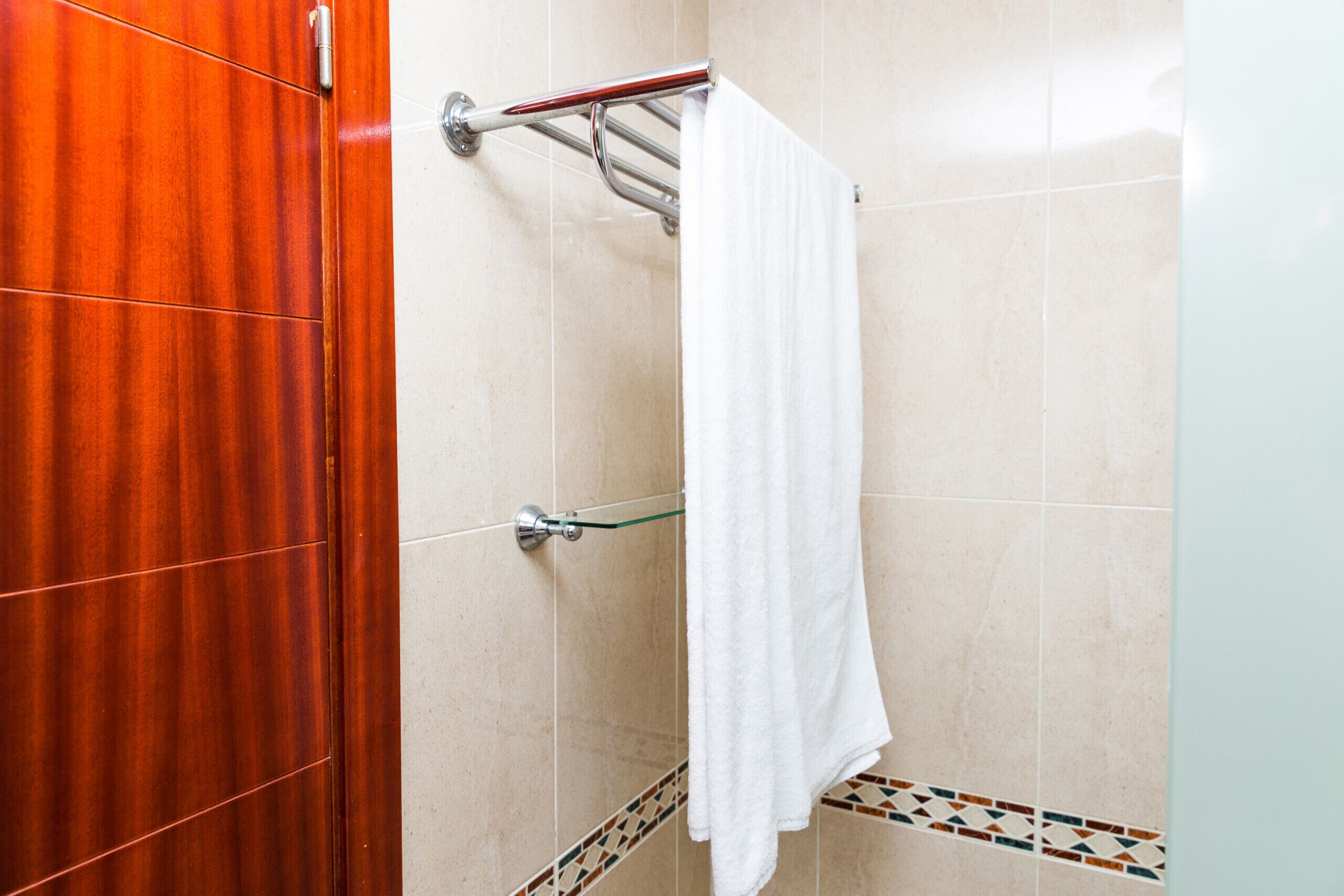 A bathroom with a wooden door, a towel rack with a white towel, and tiled walls with a decorative border.