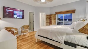 Een slaapkamer met een bed, een aan de muur bevestigde televisie, een raam met uitzicht en een plafondventilator.