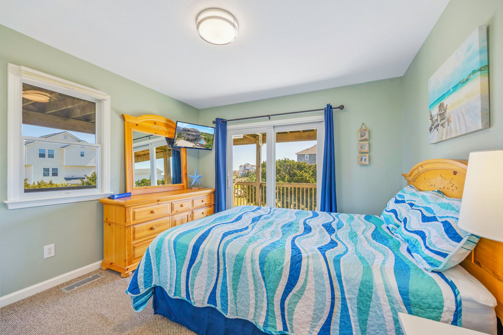 A bedroom with a bed, dresser, and a window with a view of houses.