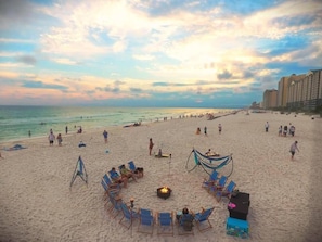 A beach with lounge chairs and a fire pit, surrounded by a row of buildings. - Tasty Waves Laketown Wharf 816-Beach Views-Beautifully Decorated!1Bd/2Ba/Sleeps 6 (Panama City Beach)