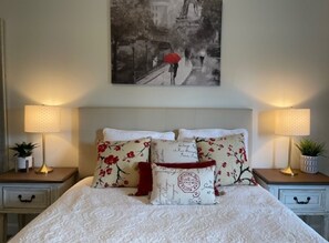 A neatly made bed with floral pillows, two bedside lamps, and a framed picture on the wall. - Paris Suite @Carolina Beach, Walk to Carolina Beach State Park (Carolina Beach)