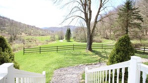 A fenced property with a gravel path leading to a grassy area and a view of a winding road in the distance. - Slatyfork Homestead - Cozy Farmhouse Near Snowshoe (Pocahontas County)