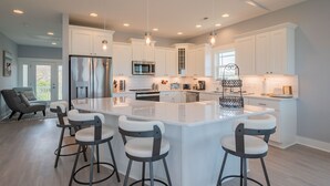 A modern kitchen with a large island, bar stools, and built-in appliances. - Sweet Sunshine: Lovely Rental with Pool and Elevator Built in 2021 (Oak Island)