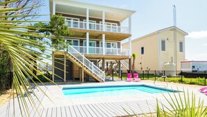 A two-story building with a wooden deck and a swimming pool. - Sweet Sunshine: Lovely Rental with Pool and Elevator Built in 2021 (Oak Island)