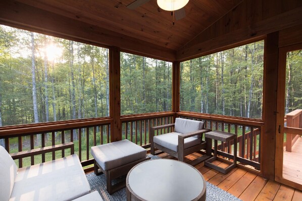 Relax on the deck with a view of the surrounding forest, surrounded by a round table and two cushioned chairs.