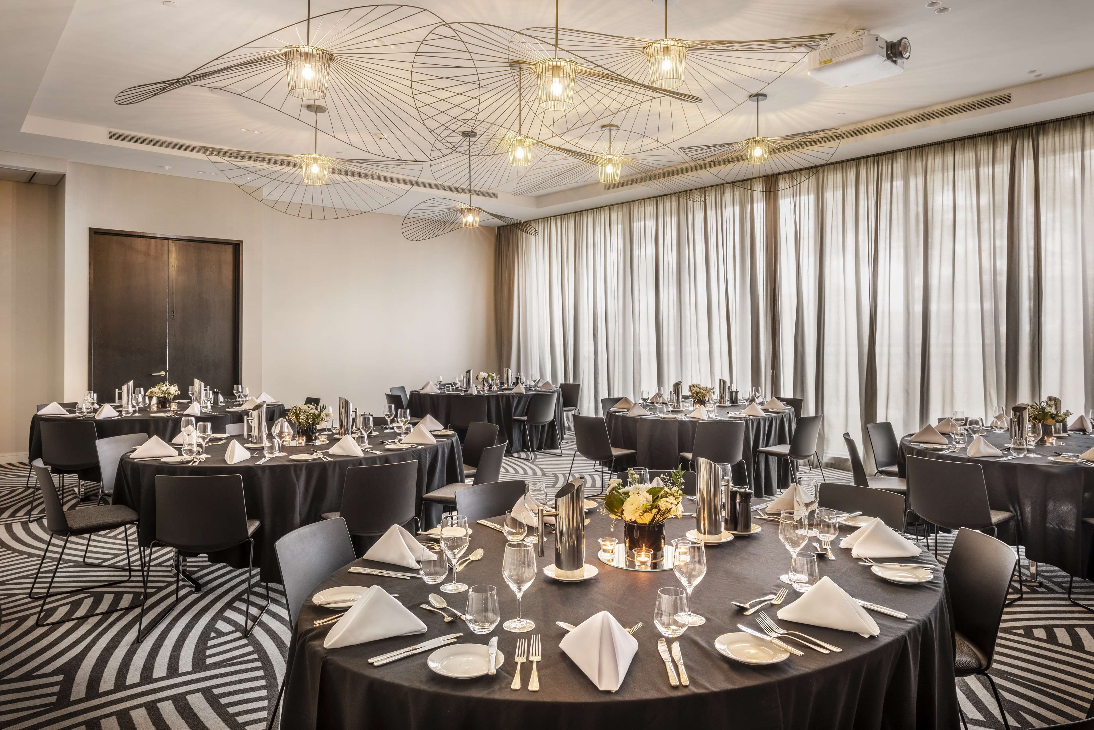 Een congreszaal met meerdere ronde tafels gedekt voor een maaltijd, met zwarte tafelkleden, witte servetten en bestek.
