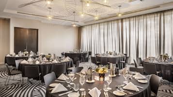 Een congreszaal met meerdere ronde tafels gedekt voor een maaltijd, met zwarte tafelkleden, witte servetten en bestek.