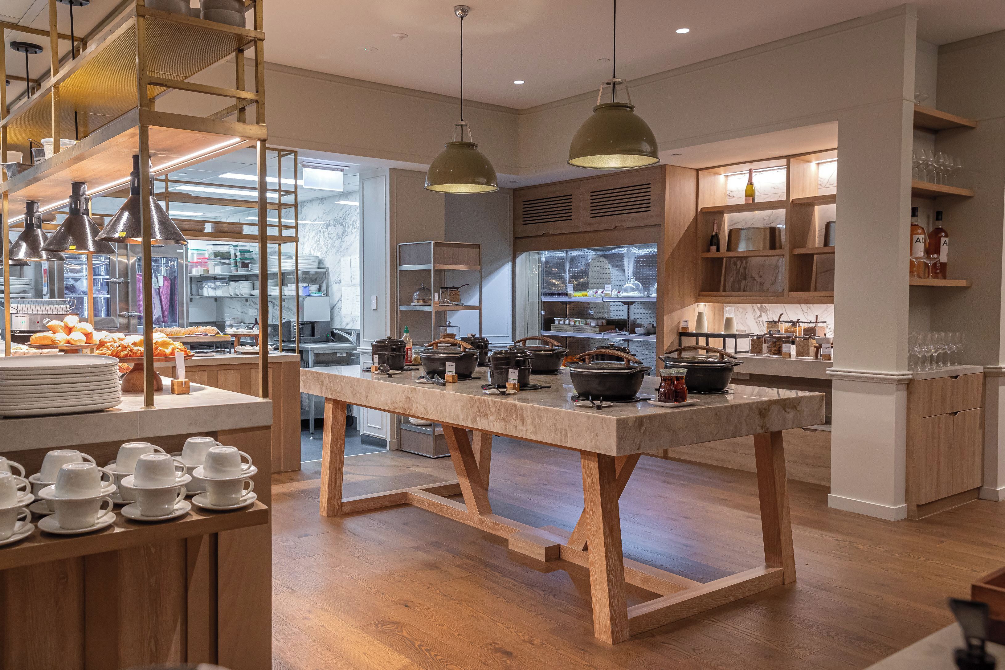 A modern kitchen with wooden tables, hanging pendant lights, and a variety of kitchenware.