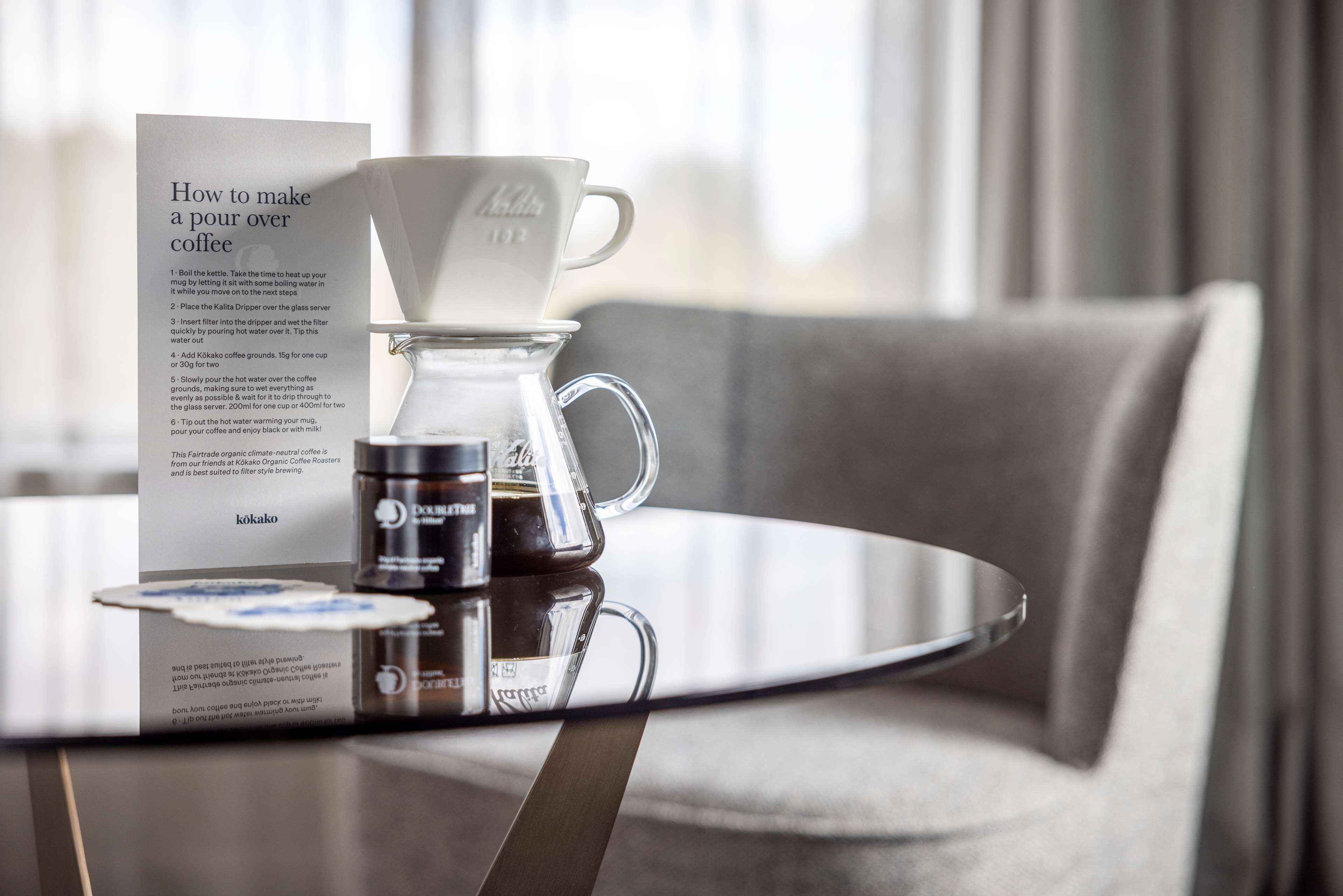 Un appareil à café comprenant une verseuse en verre, une tasse en papier et une dosette de café, le tout posé sur une table.