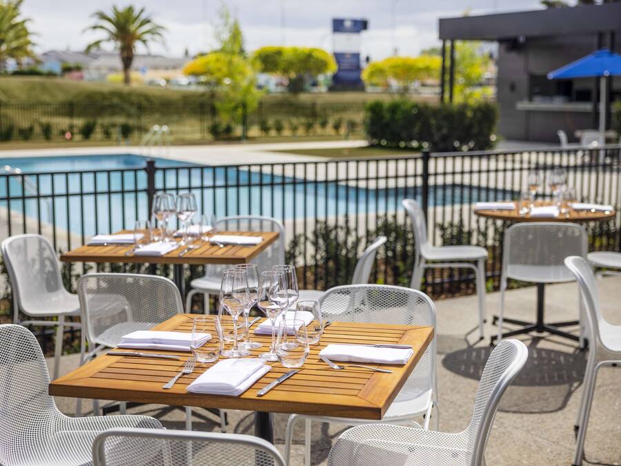 Outdoor dining tables with chairs, a pool, and a fence.