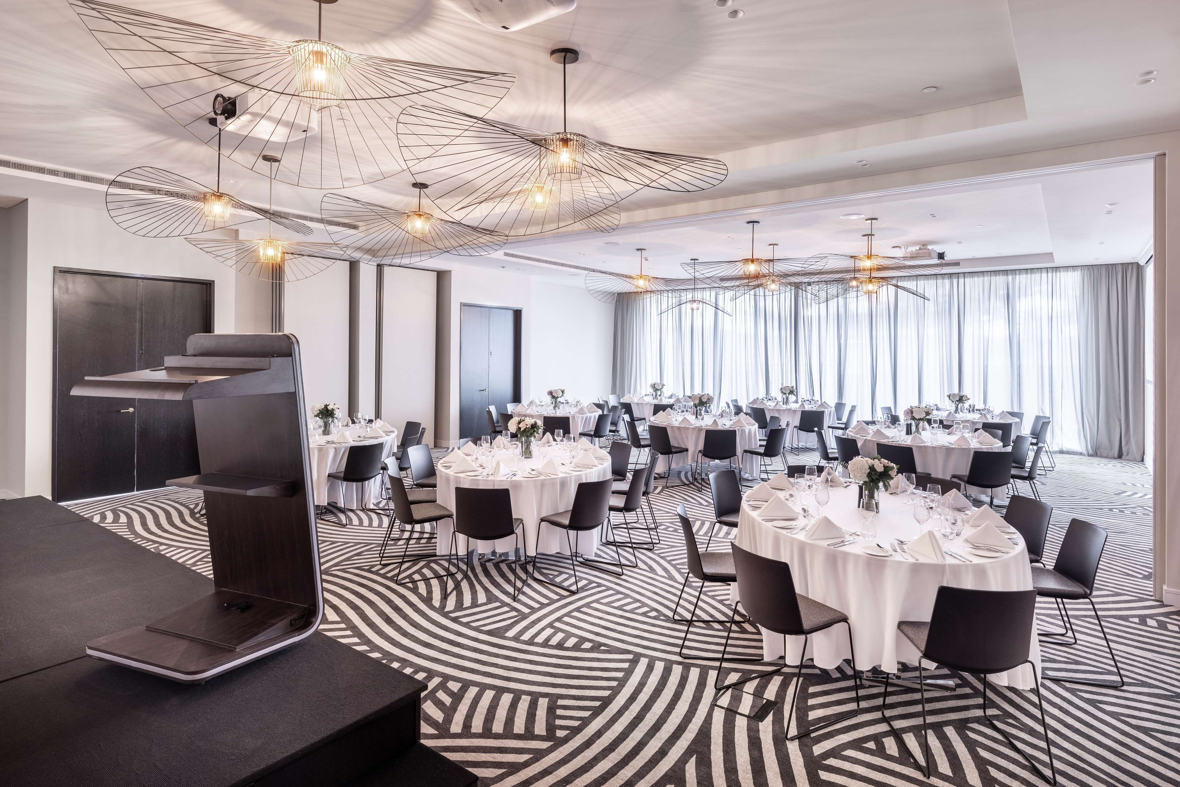 A modern conference room with round tables, black chairs, and a unique ceiling design.