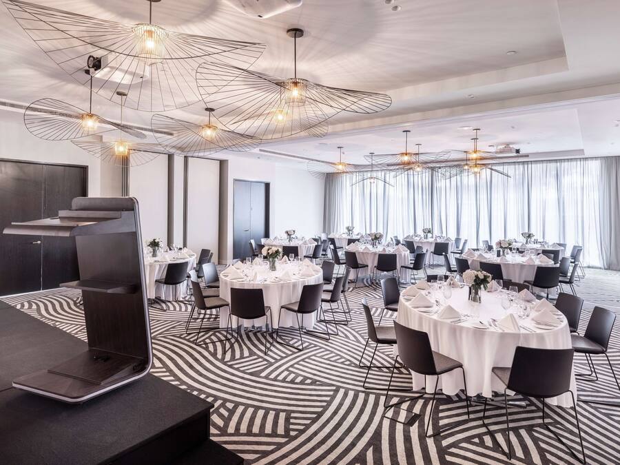 A modern conference room with round tables, black chairs, and a unique ceiling design.