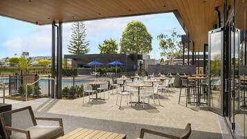 An outdoor patio area with tables and chairs, a pool, and a view of the cityscape.