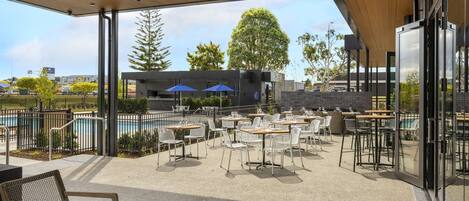 An outdoor patio area with tables and chairs, a pool, and a view of the cityscape.