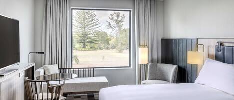 Habitación de hotel con una ventana grande, una cama, un escritorio con una silla, un sofá y una lámpara.