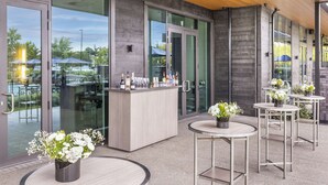 A modern outdoor seating area with a bar, glass doors, and potted plants. - DoubleTree by Hilton Auckland Karaka (Karaka)