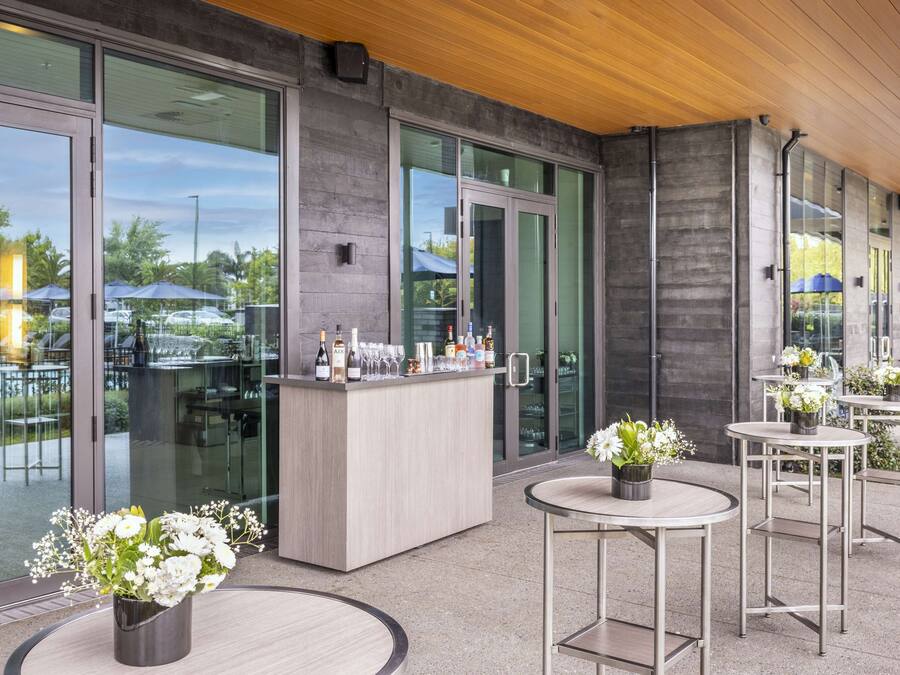 A modern outdoor seating area with a bar, glass doors, and potted plants.