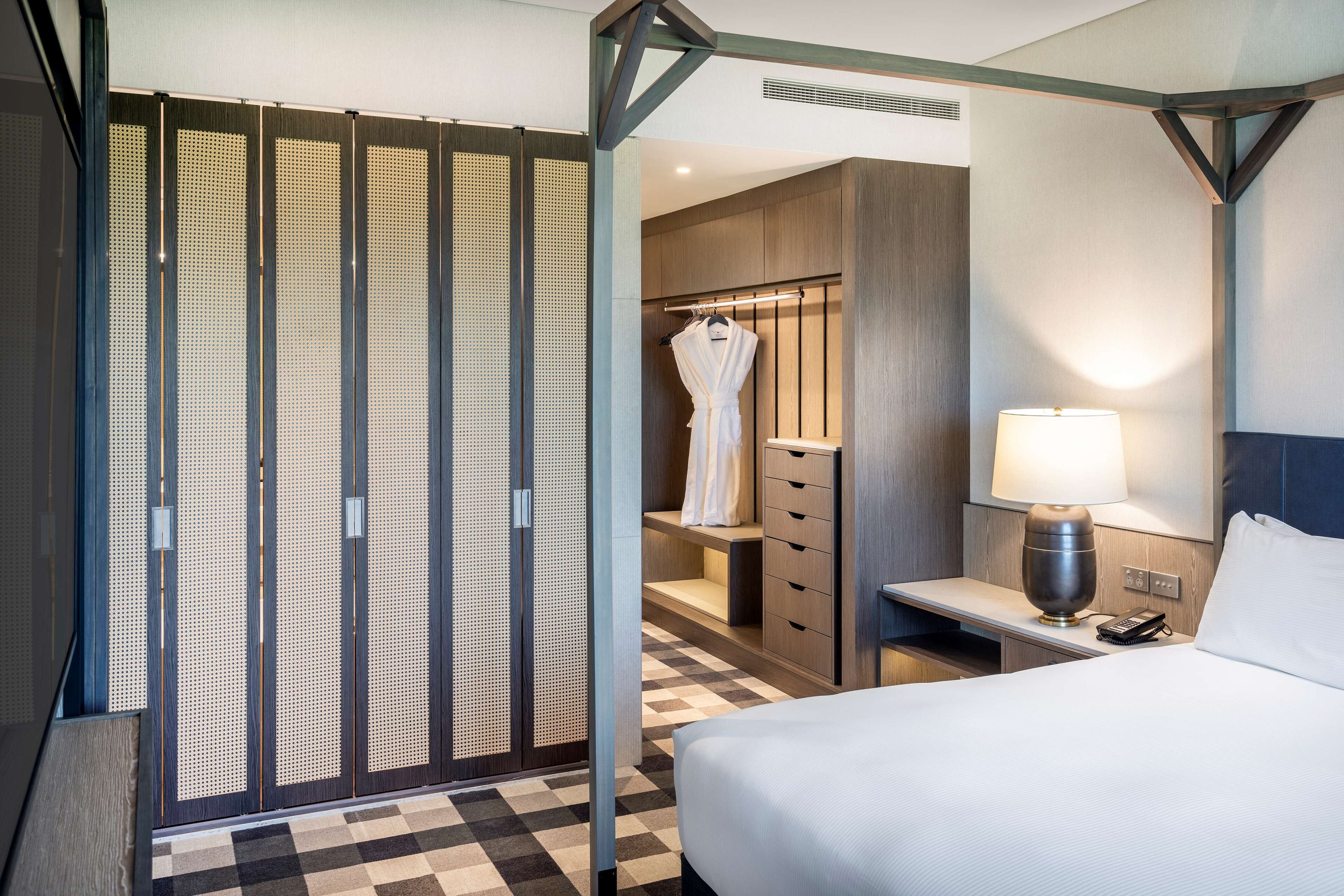 Habitación de hotel con cama, mesita de noche, lámpara, bata y armario.