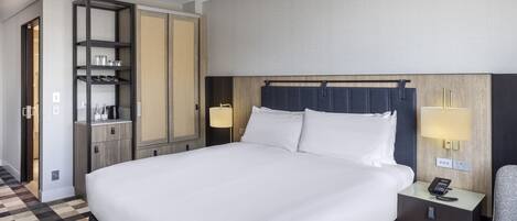 A hotel room with a large bed, a bedside table with a lamp, a wardrobe, and a chair.