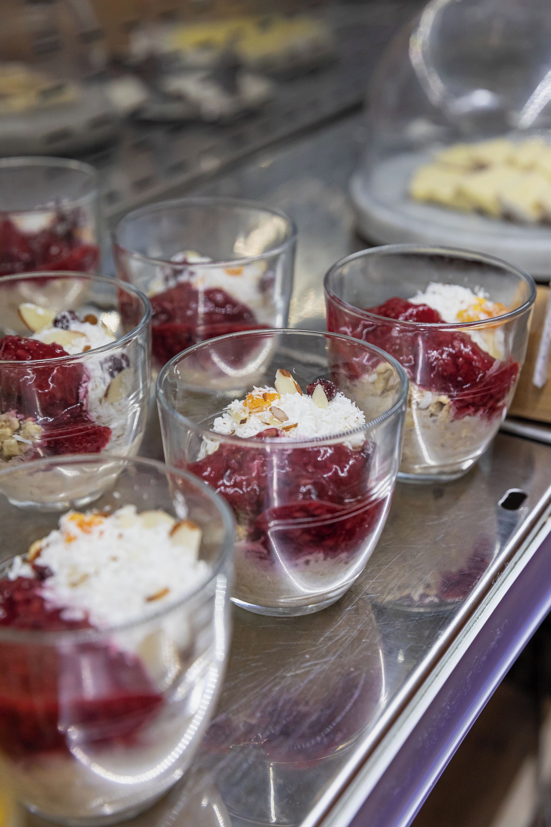 A tray with several glass cups containing layered desserts with fruits and coconut flakes.