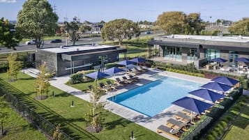 A modern hotel with a swimming pool, lounge chairs, and umbrellas.
