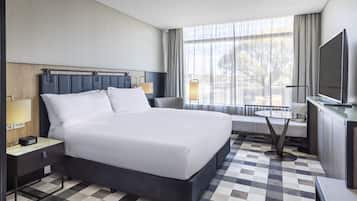 A modern hotel room with a large bed, bedside tables, a TV, and a view of the outdoors.