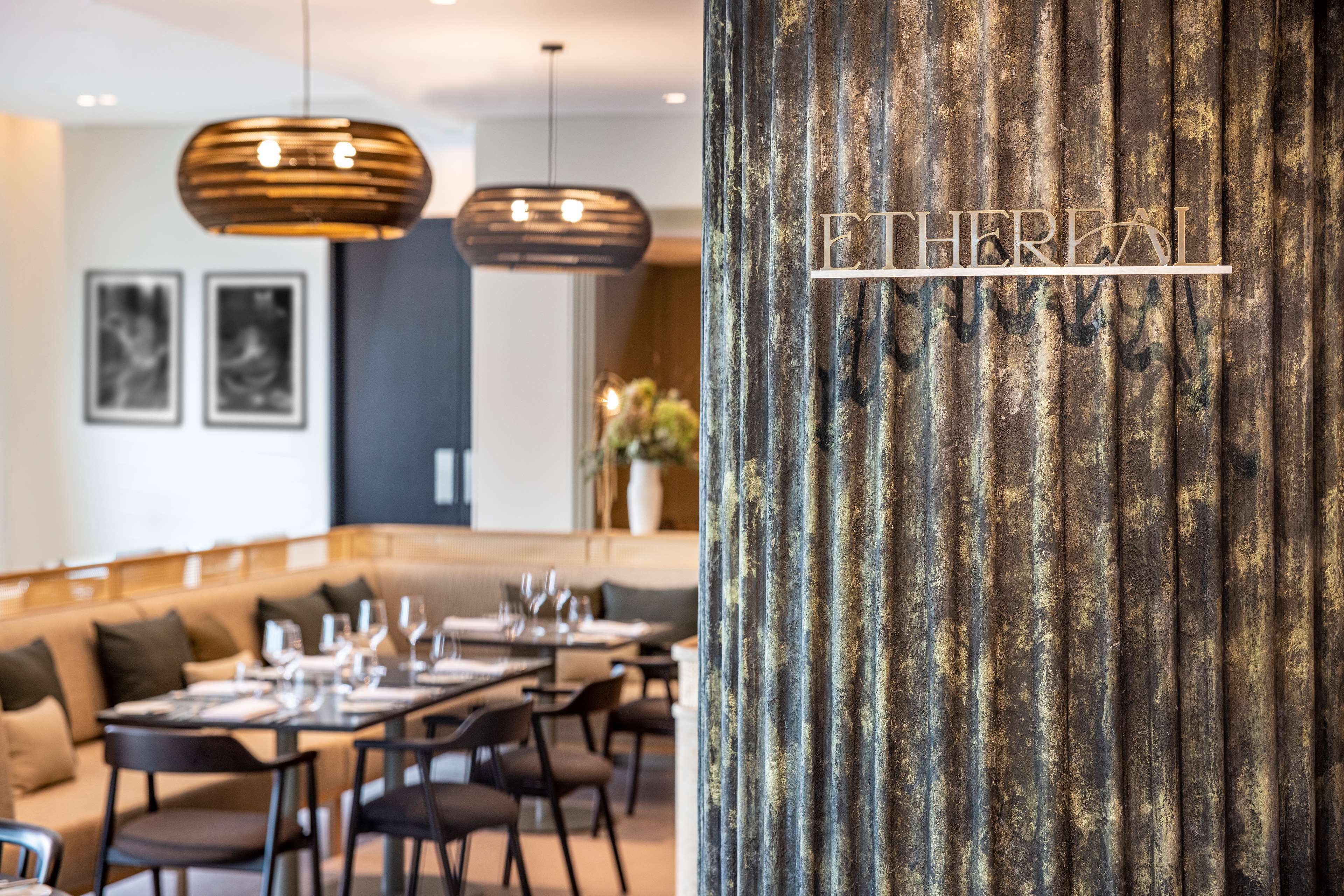 A restaurant with a modern interior, featuring a long dining table, multiple chairs, and hanging pendant lights.