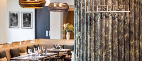 Un restaurant au décor moderne, avec une longue table à manger, de nombreuses chaises et des lampes suspendues.