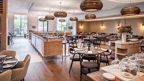 A spacious restaurant with multiple dining tables and chairs, a central bar area, and pendant lighting. - DoubleTree by Hilton Auckland Karaka (Karaka)