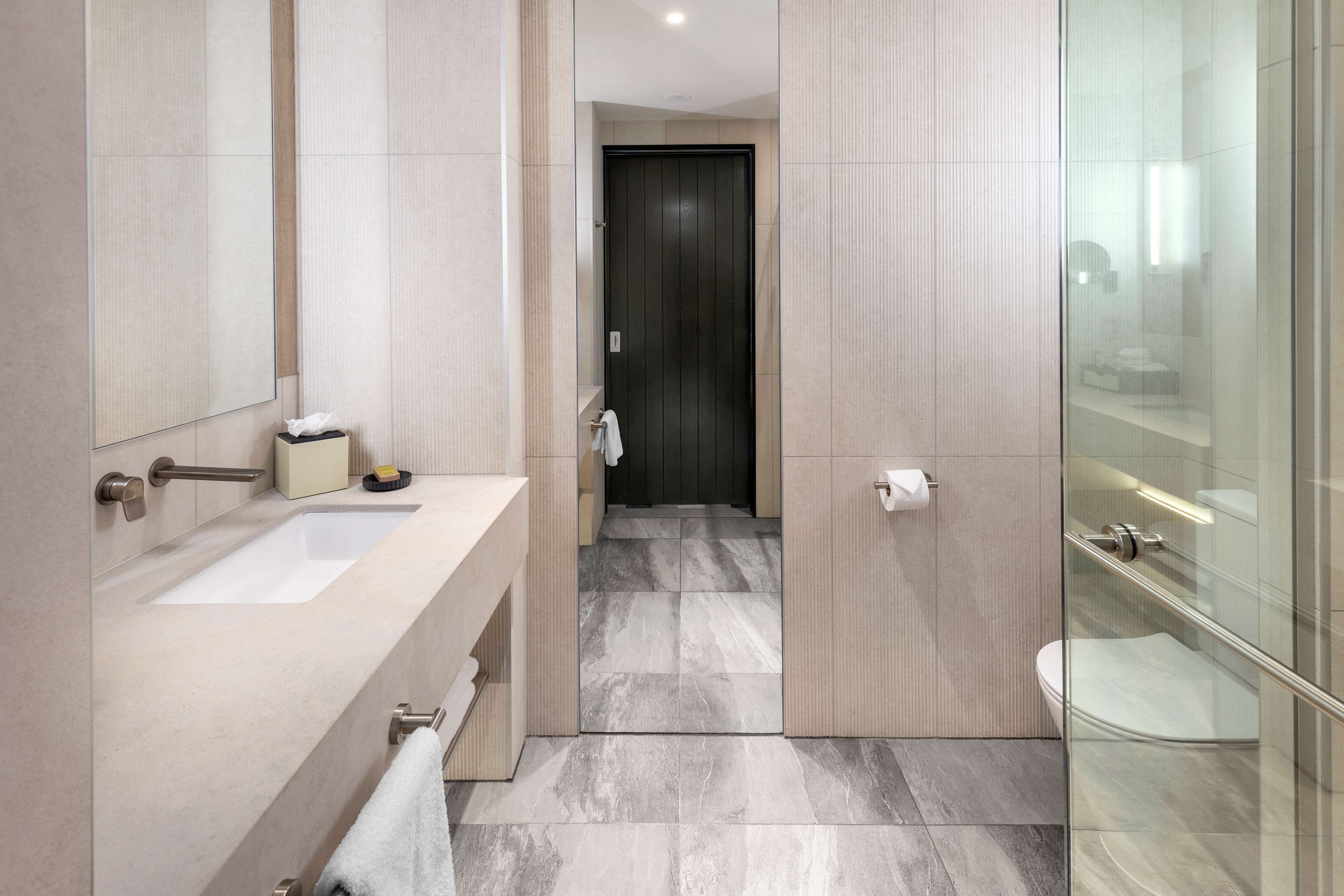 A modern bathroom with a large mirror, a sink, a toilet, and a glass shower enclosure.