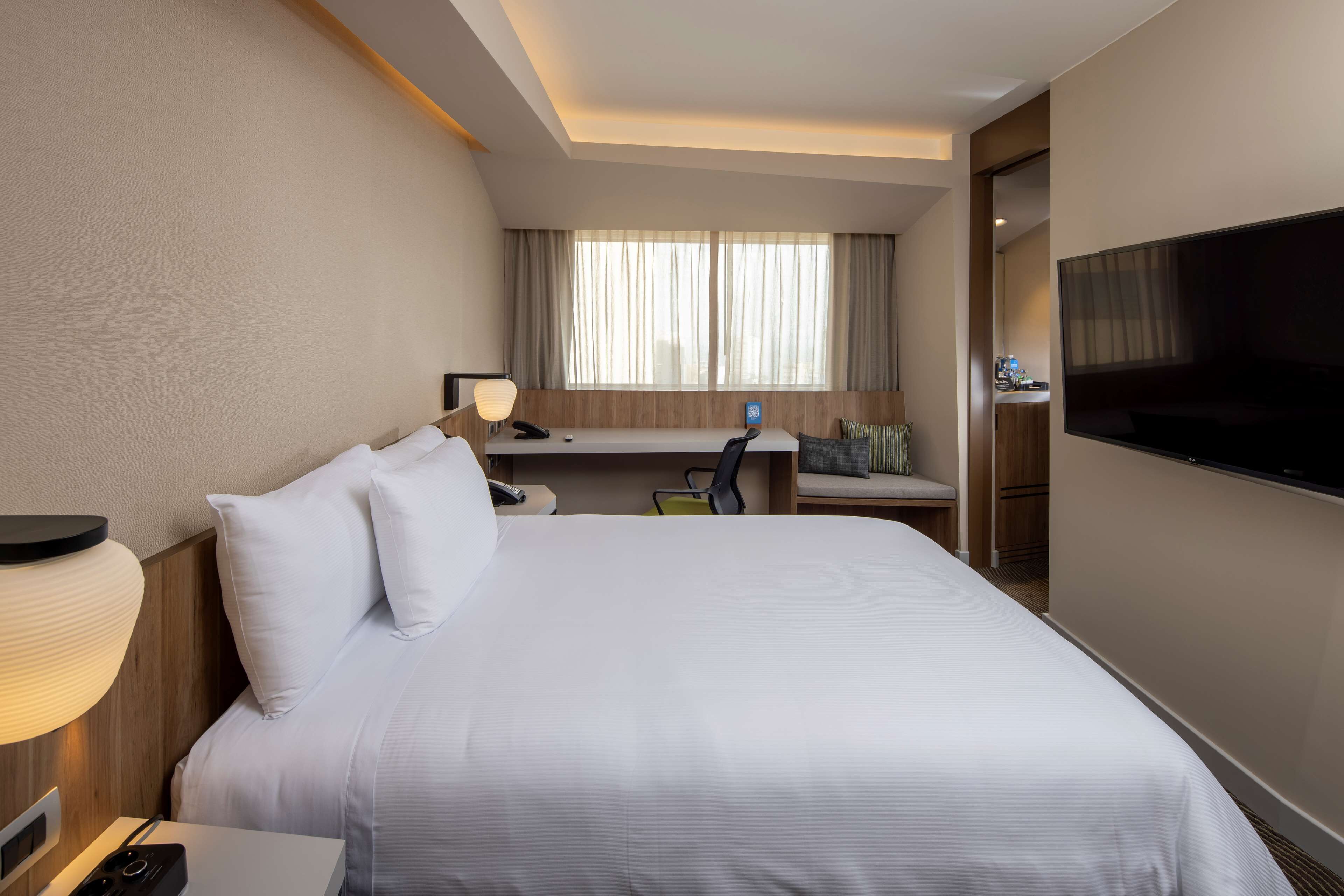Habitación de hotel con una cama grande, un escritorio con silla, un televisor y una ventana con cortinas.
