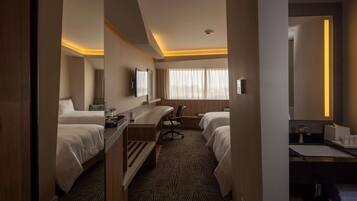Habitación de hotel con dos camas, un escritorio, una silla, un espejo grande y una ventana con cortinas.