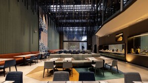 Un restaurante moderno con techos altos, un área de asientos central y vistas de la ciudad a través de amplios ventanales.