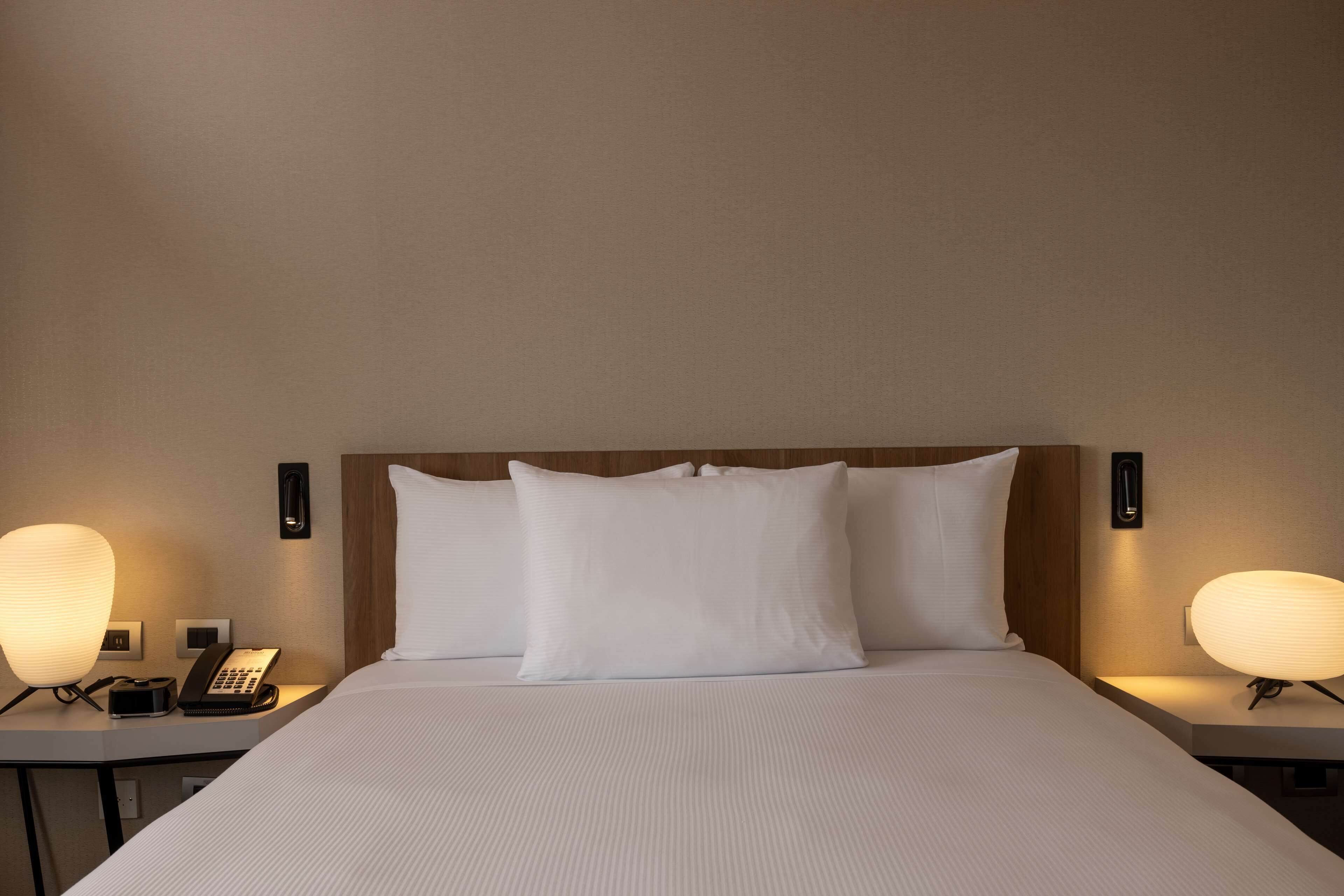 Una habitación de hotel con una cama grande, dos mesitas de noche, un teléfono y lámparas de pared.