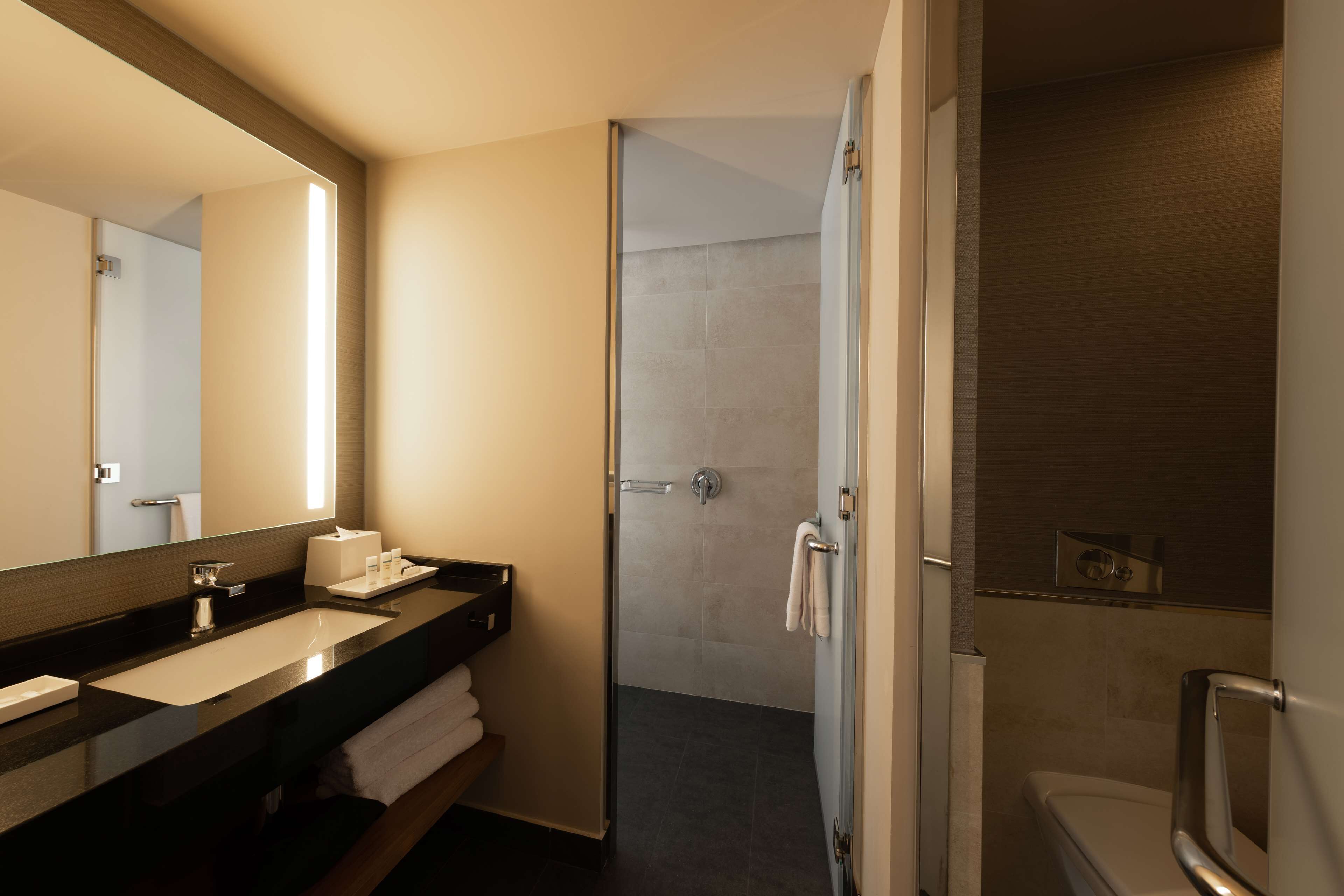 Un baño moderno con un espejo grande, un lavamanos, una ducha y un inodoro.