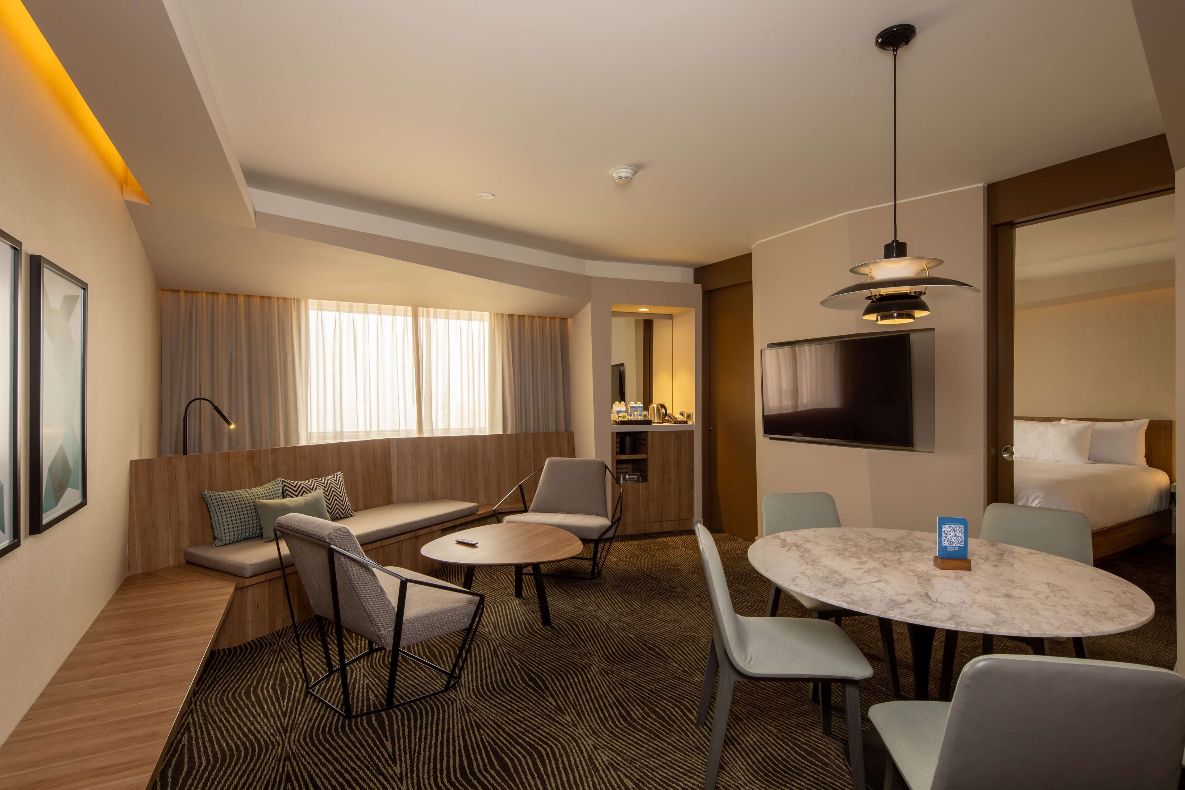 A hotel room with a seating area, a dining table, a TV, and a bed.
