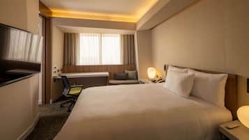A hotel room with a large bed, a desk with a chair, a TV, a window with curtains, and a bedside lamp.