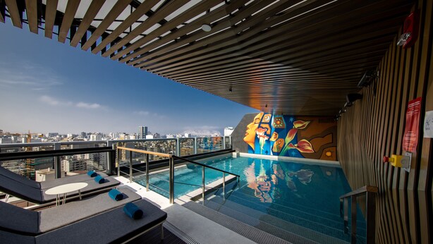 Una piscina en la azotea con vistas a la ciudad, zona de descanso y un mural.