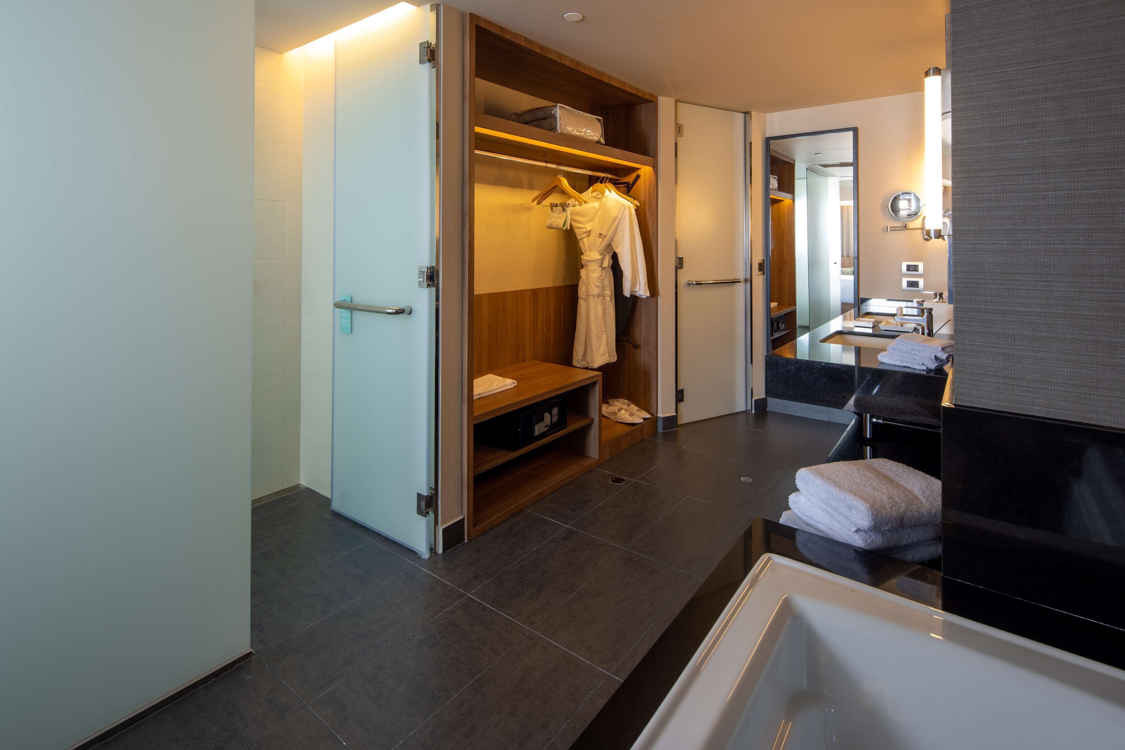 A modern bathroom with a bathtub, a vanity with a mirror, and a walk-in closet with hanging robes.