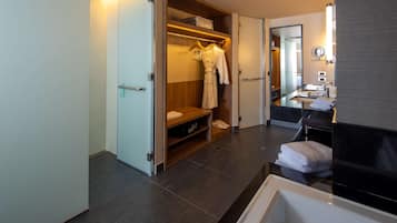 A modern bathroom with a bathtub, a vanity with a mirror, and a walk-in closet with hanging robes.