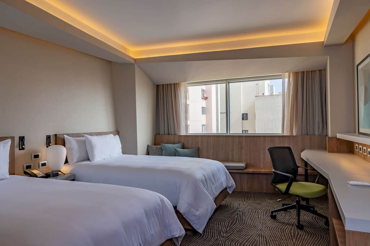 A hotel room with two beds, a desk, a chair, a telephone, and a window with curtains.