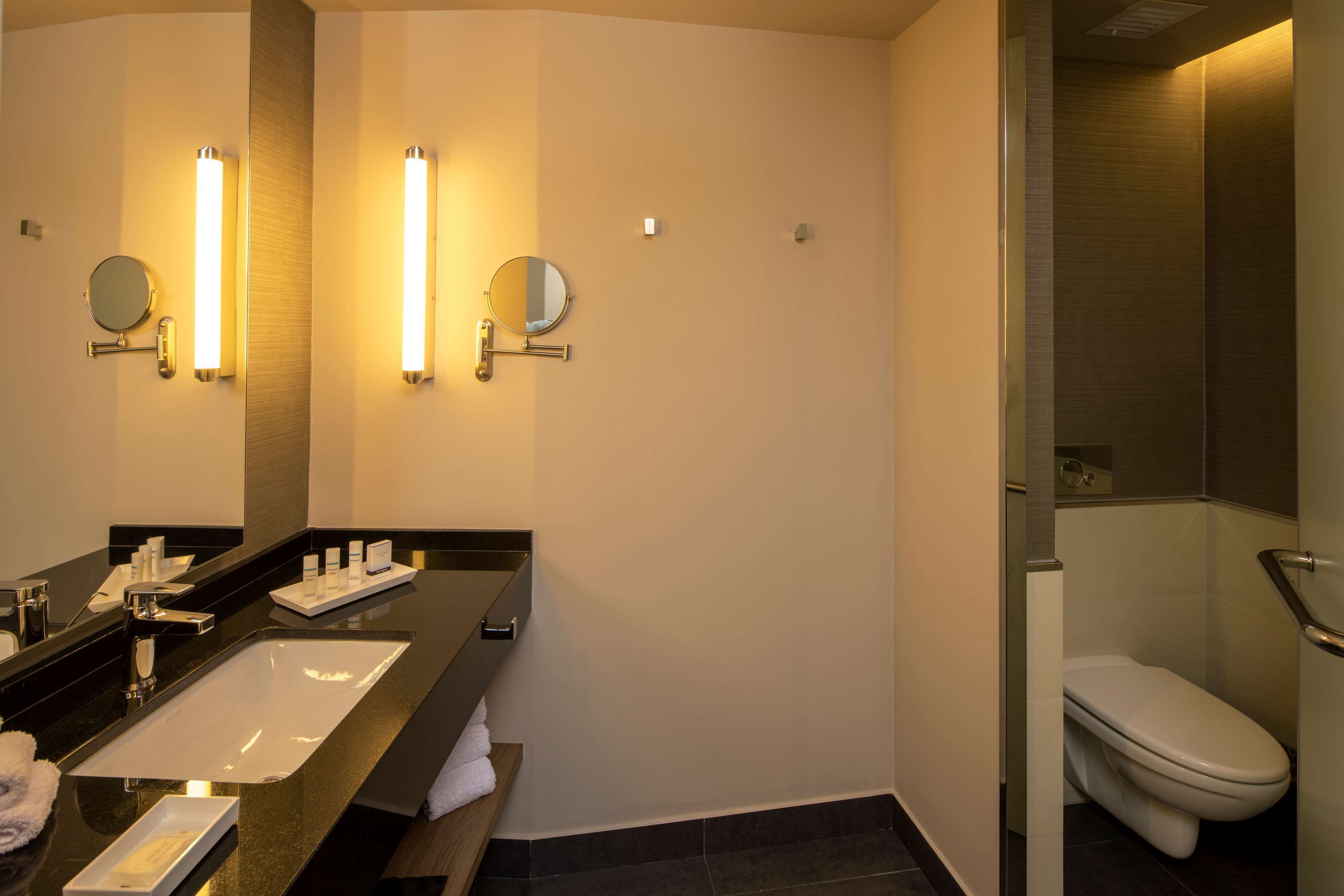 Un baño moderno con encimera negra, lavamanos blanco, dos espejos montados en la pared y un inodoro.
