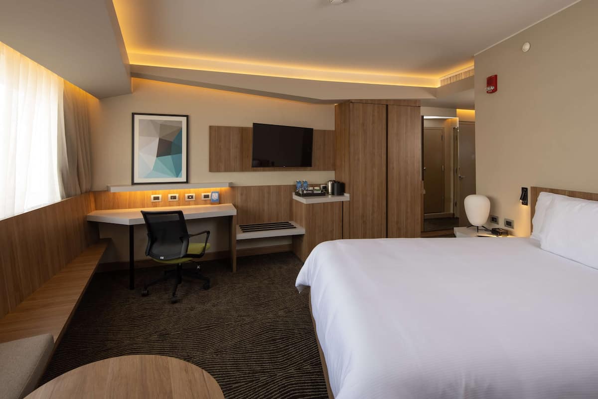 A hotel room with a bed, desk, chair, TV, and a bathroom door.